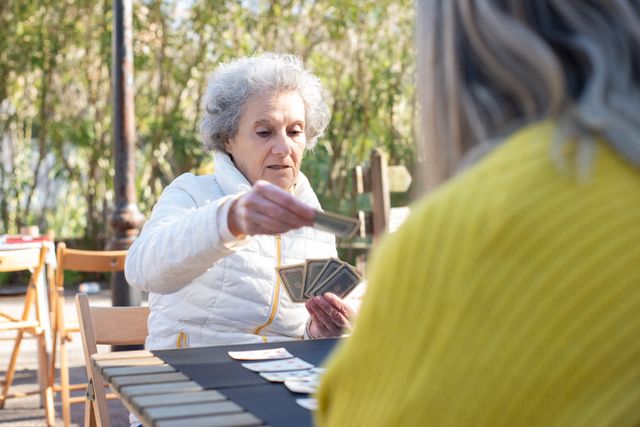 une senior en pull blanc qui joue aux cartes en extérieur, activités seniors 